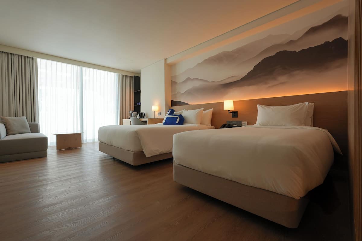 Ett hotellrum med två sängar, en soffa och ett stort fönster med gardiner.