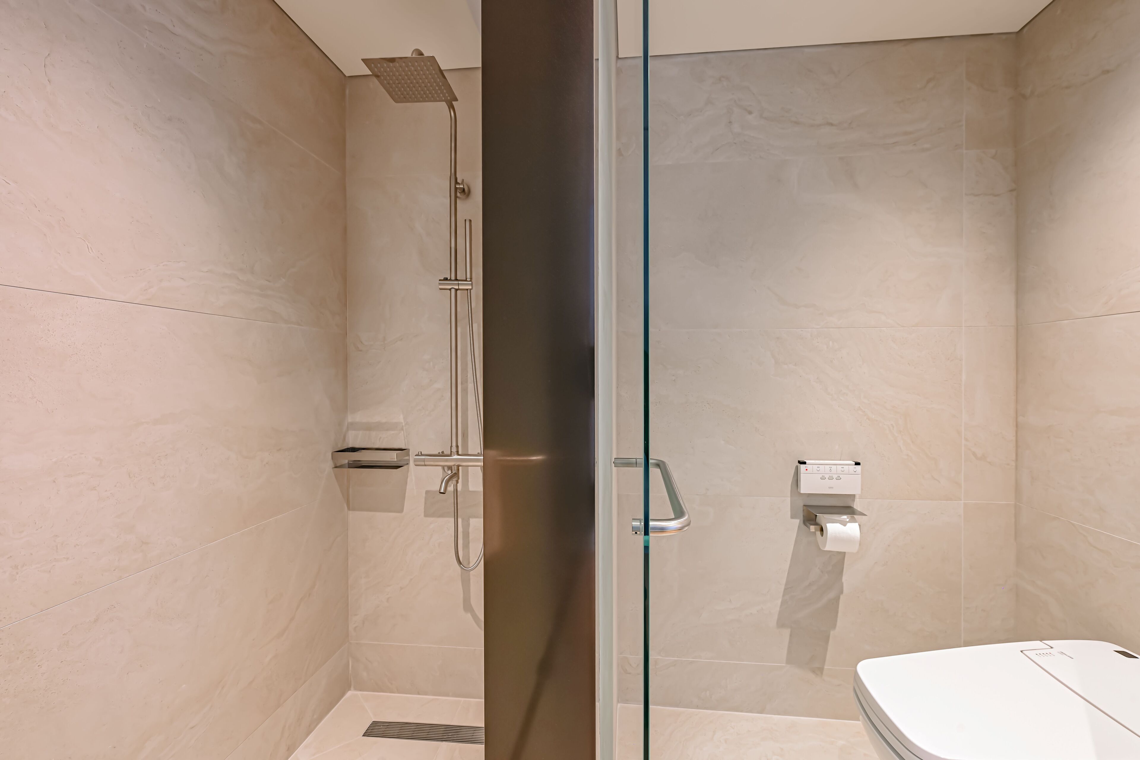 A modern bathroom with a glass shower enclosure, a toilet, and a paper towel dispenser.