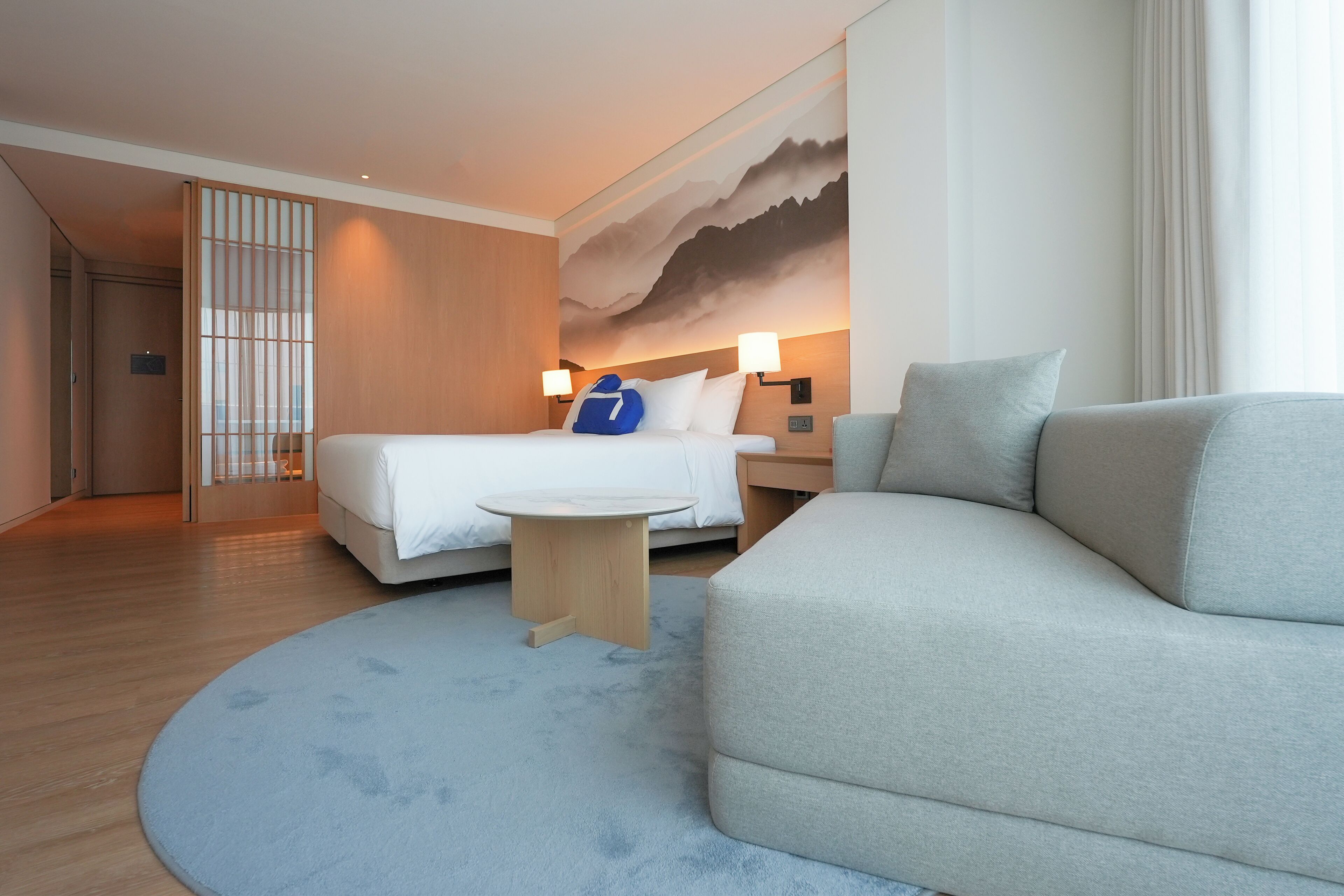 Una habitación de hotel moderna con una cama, un sofá, una mesita y un cuadro grande en la pared.