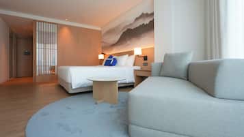 Una habitación de hotel moderna con una cama, un sofá, una mesita y un cuadro grande en la pared.