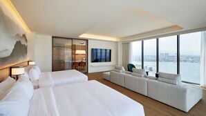 Habitación de hotel con dos camas, un sofá, televisión y vistas a la ciudad.