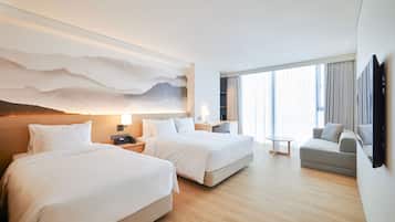A hotel room with two beds, a desk, a chair, and a large window with curtains.