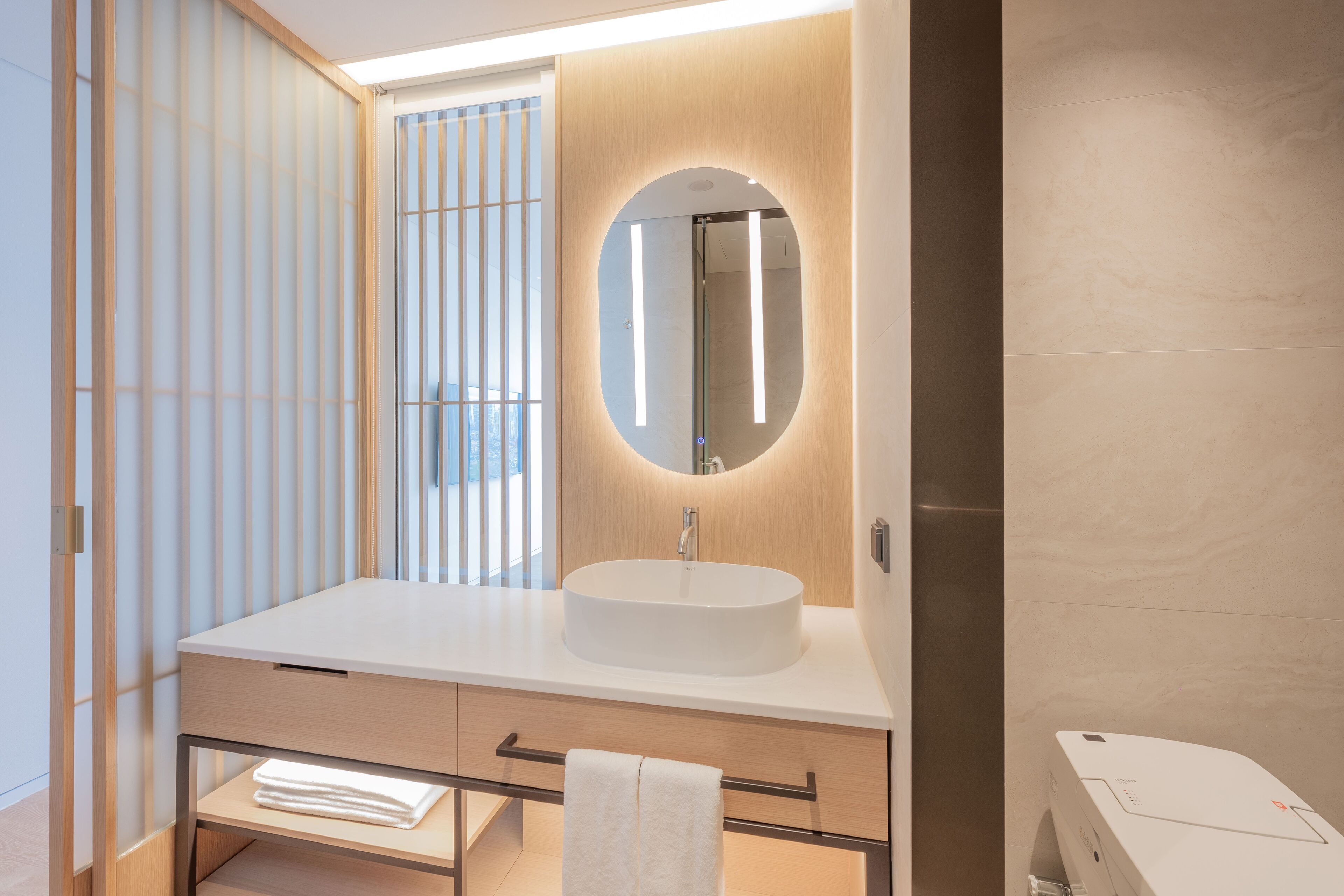 Un baño moderno con un espejo redondo, un lavabo blanco y un perchero para toallas.