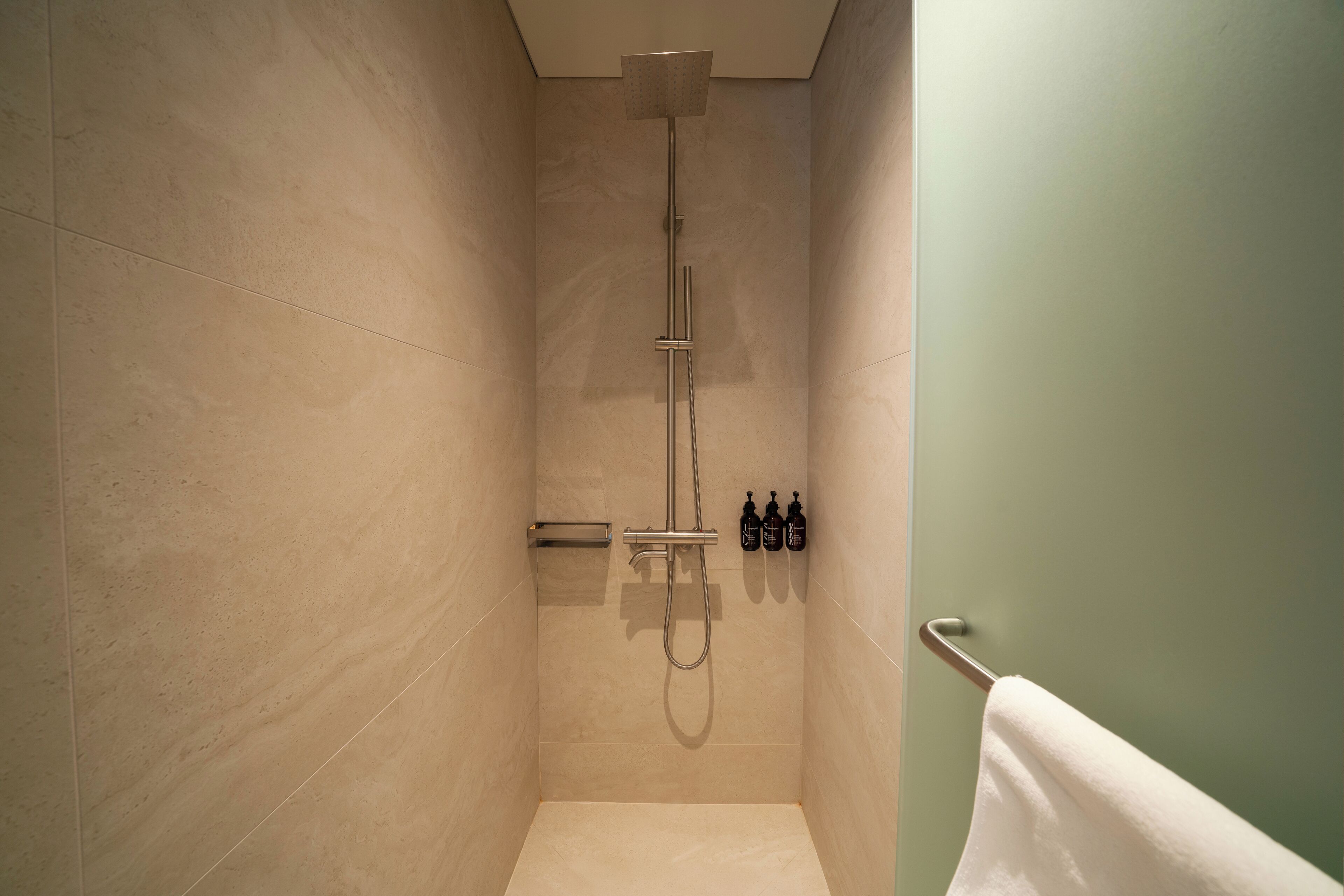 A modern shower with a handheld showerhead, a wall-mounted faucet, and a towel rack with a white towel.