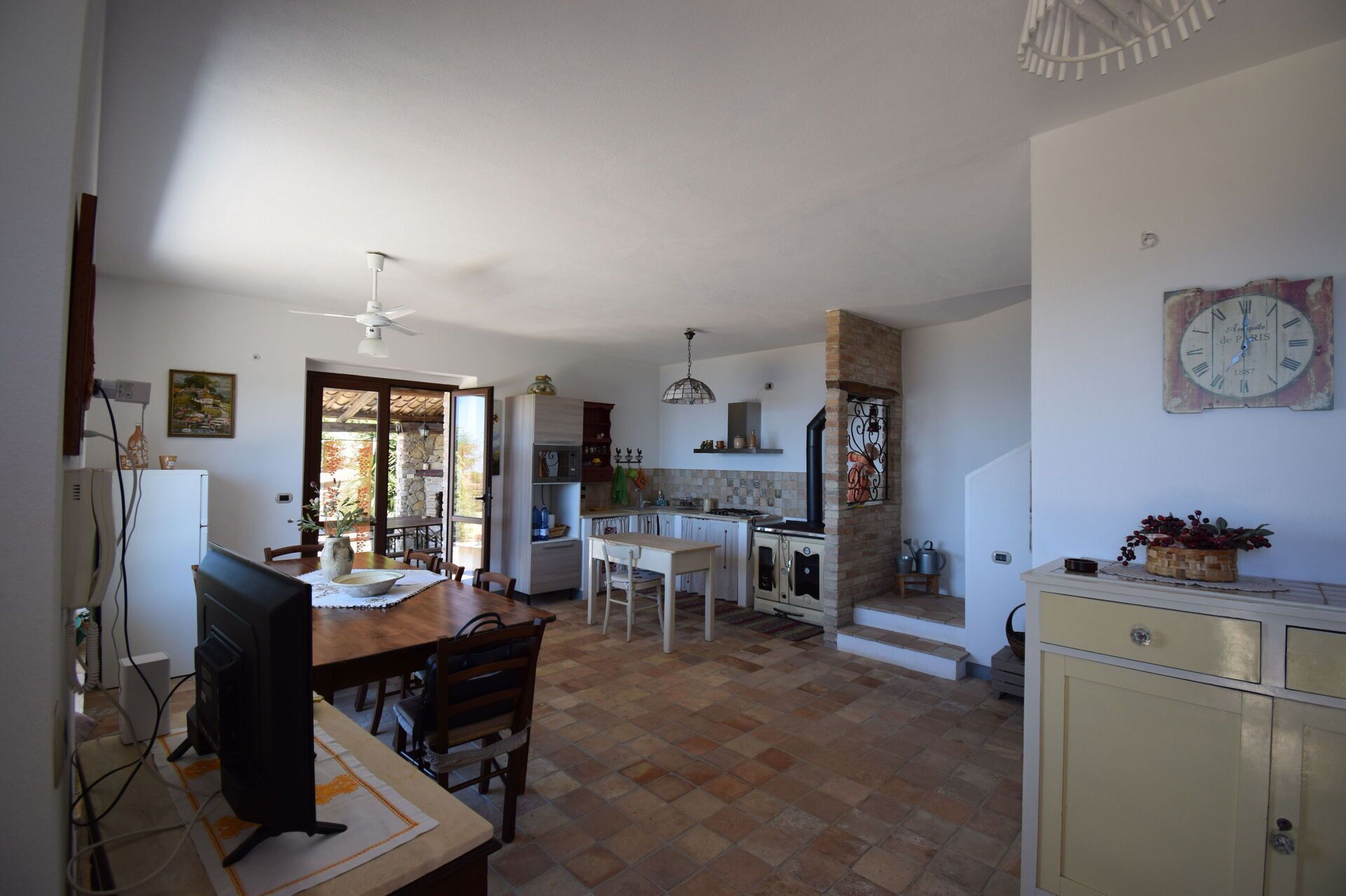 Una cocina amplia con comedor, que presenta una pared de piedra, suelo de baldosas y un reloj en la pared.