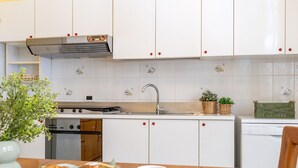 Een keuken met witte kasten, een roestvrijstalen afzuigkap, een spoelbak en een kookplaat. Op het aanrecht staan twee manden met planten.