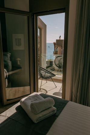 A hotel room with a bed, a window with curtains, a view of the sea, and a chair outside.