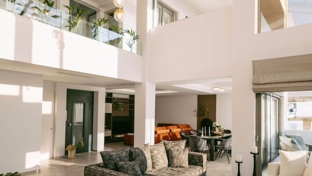 Un vaste espace de vie doté d’un haut plafond, comprenant un ensemble de canapés, une table basse et un coin repas avec une table et des chaises.