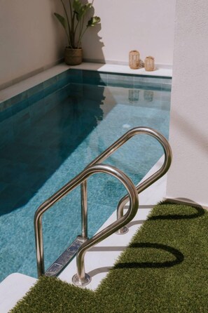 Una piscina con barandilla de metal, una planta en maceta y una pequeña mesa con velas.