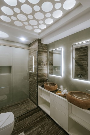 Un bagno moderno con un mobile contenitore in legno, due lavandini rotondi, uno specchio grande e controsoffitti con faretti circolari.