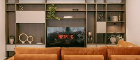 Una sala de estar con un televisor de pantalla plana grande, un sofá y estanterías empotradas con objetos decorativos.