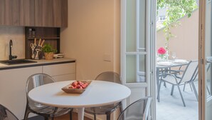 A modern kitchen with a white countertop, a sink, and a dining area with a round table and chairs. - Como Liberty Suites - Gatsby (Como)