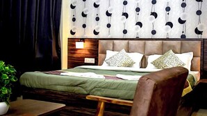 A hotel room with a large bed, a bedside table, a nightstand, and a wall with a unique pattern. - Hotel Panchvati (Malangawa)