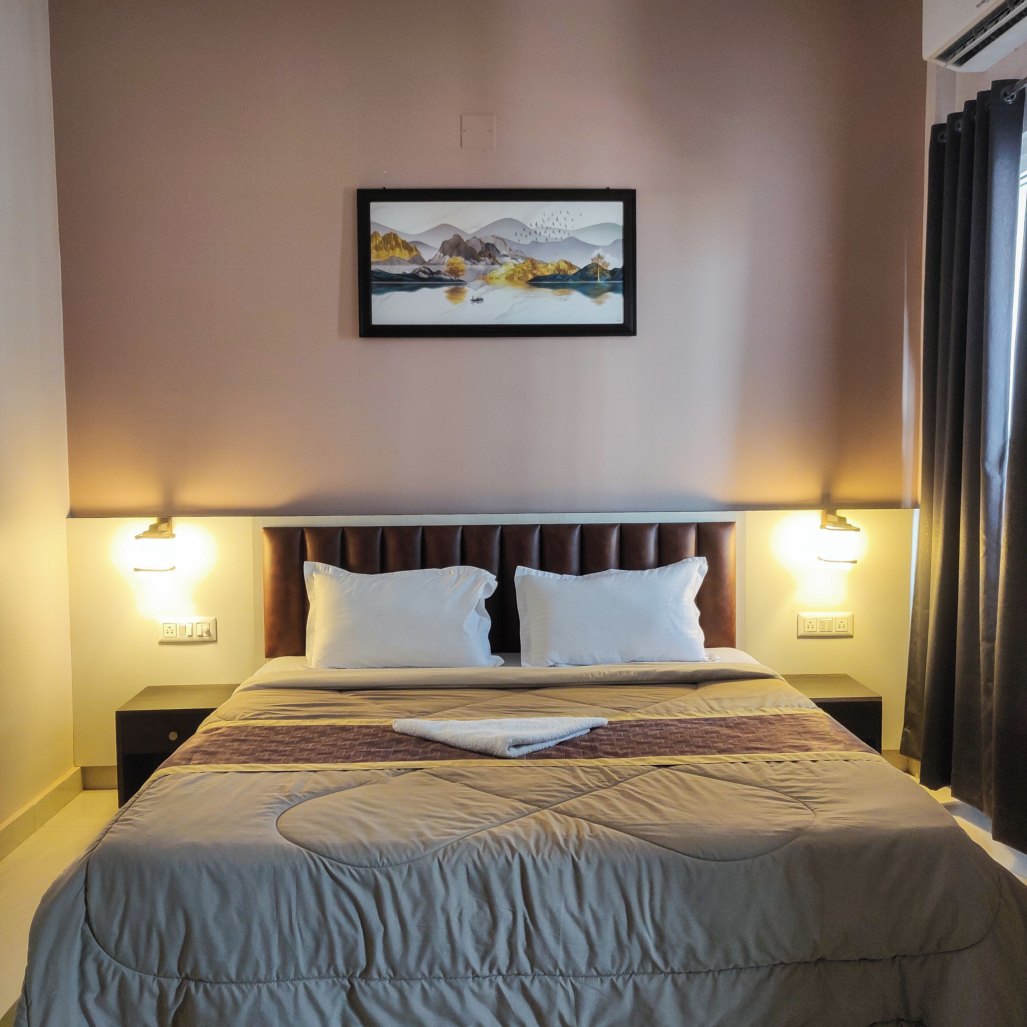 A neatly made bed with a headboard, two bedside lamps, and a framed picture on the wall.