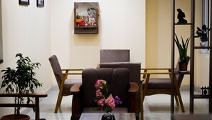 A room with a brown armchair, a small table with a vase of flowers, a shelf with decorative items, and a potted plant. - Hotel Panchvati (Malangawa)