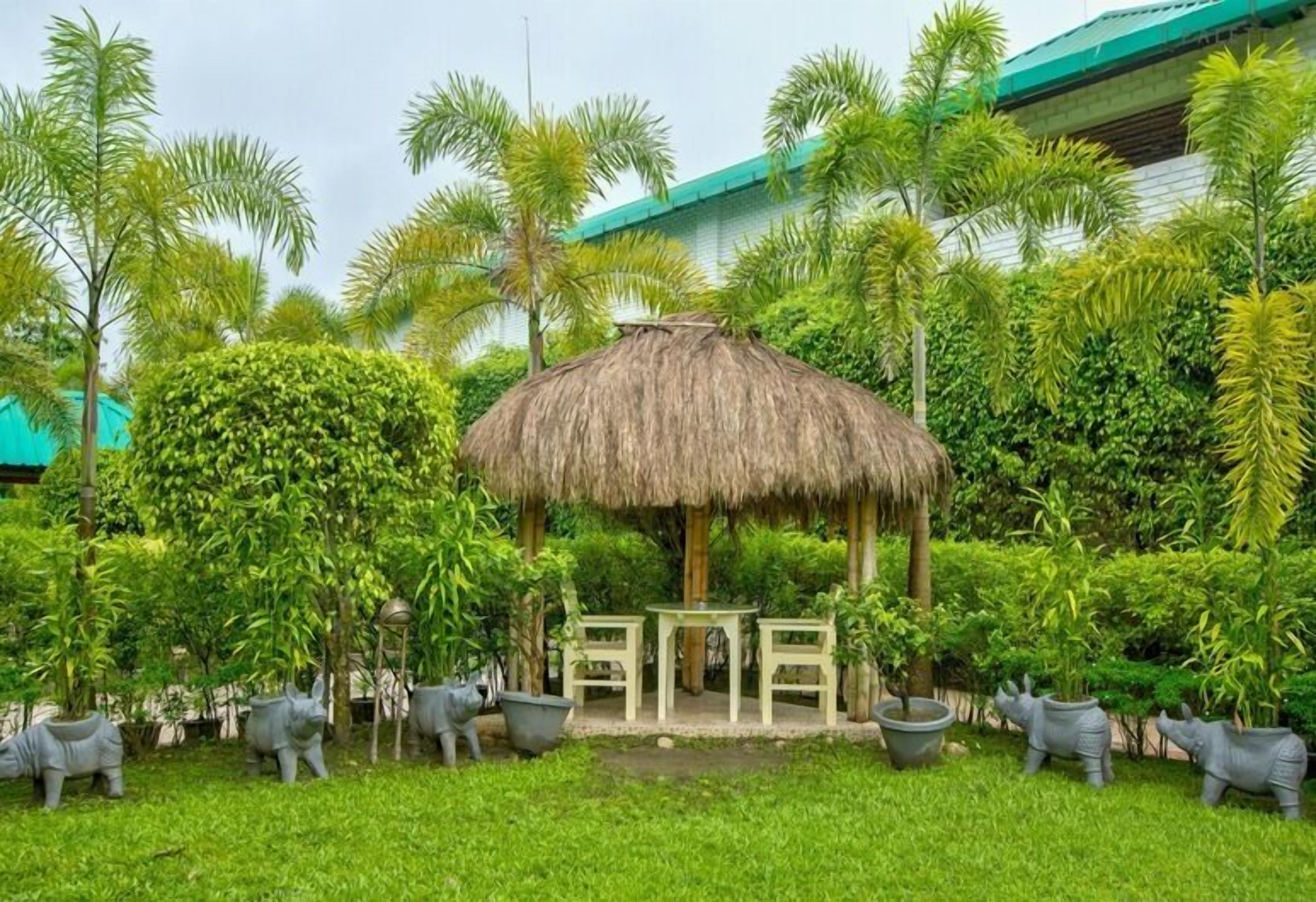 A thatched-roof gazebo with a table and chairs in a lush garden setting.