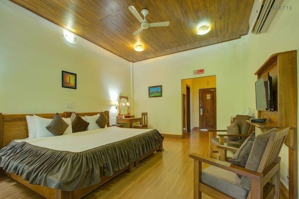 A hotel room with a large bed, wooden furniture, a ceiling fan, and a television.