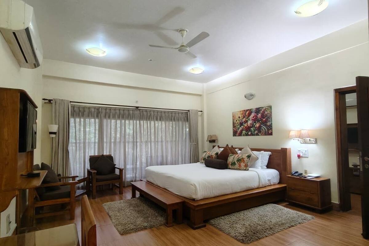 A bedroom with a bed, bedside tables, a desk, a chair, a ceiling fan, and a window with curtains.