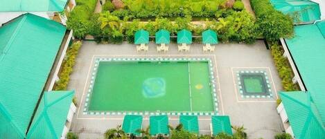 Un patio con un césped central, rodeado de árboles y una zona de piscina con tumbonas.