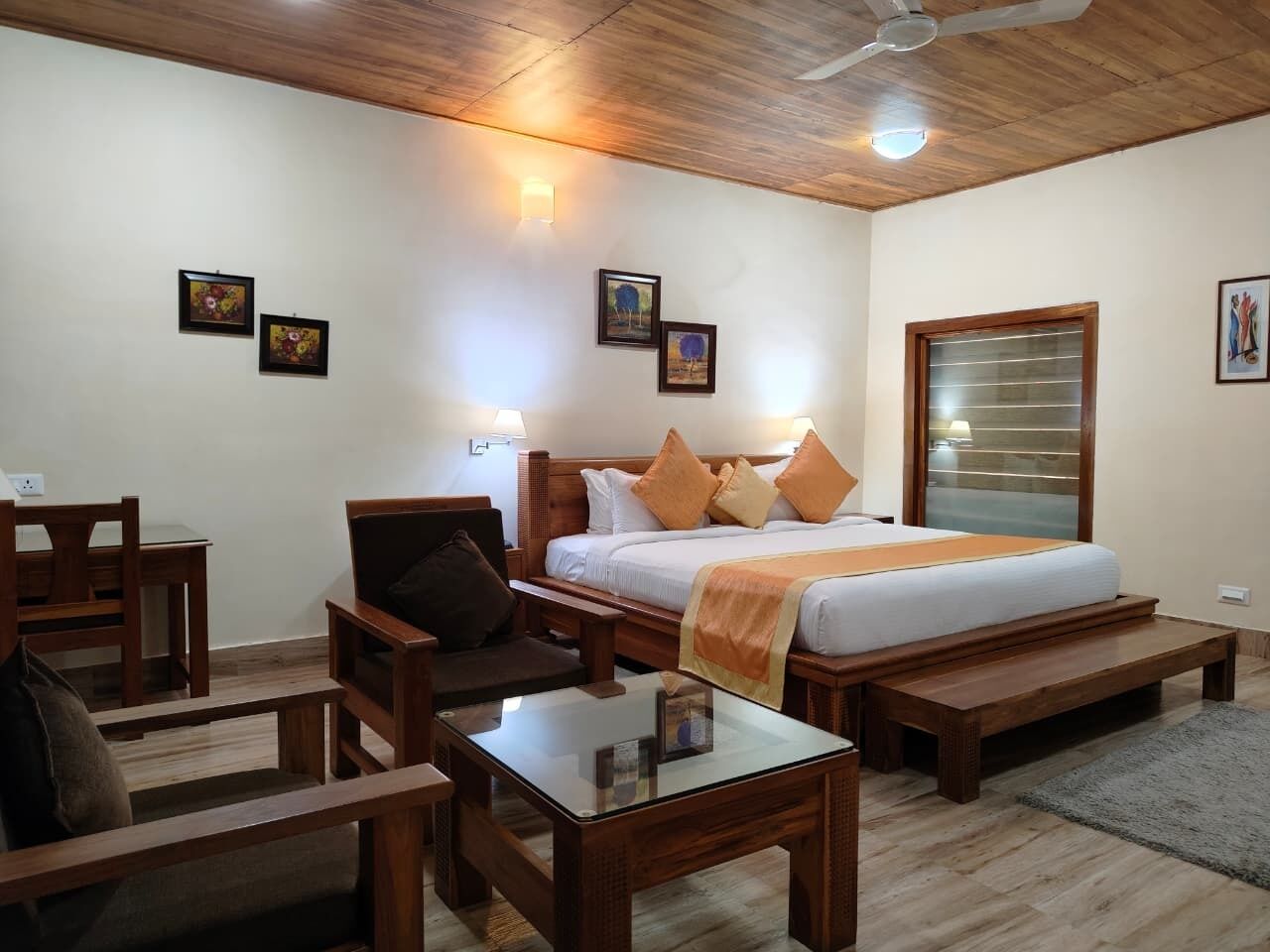A hotel room with a wooden ceiling, a bed with orange and white bedding, a wooden desk, a chair, and a small table.