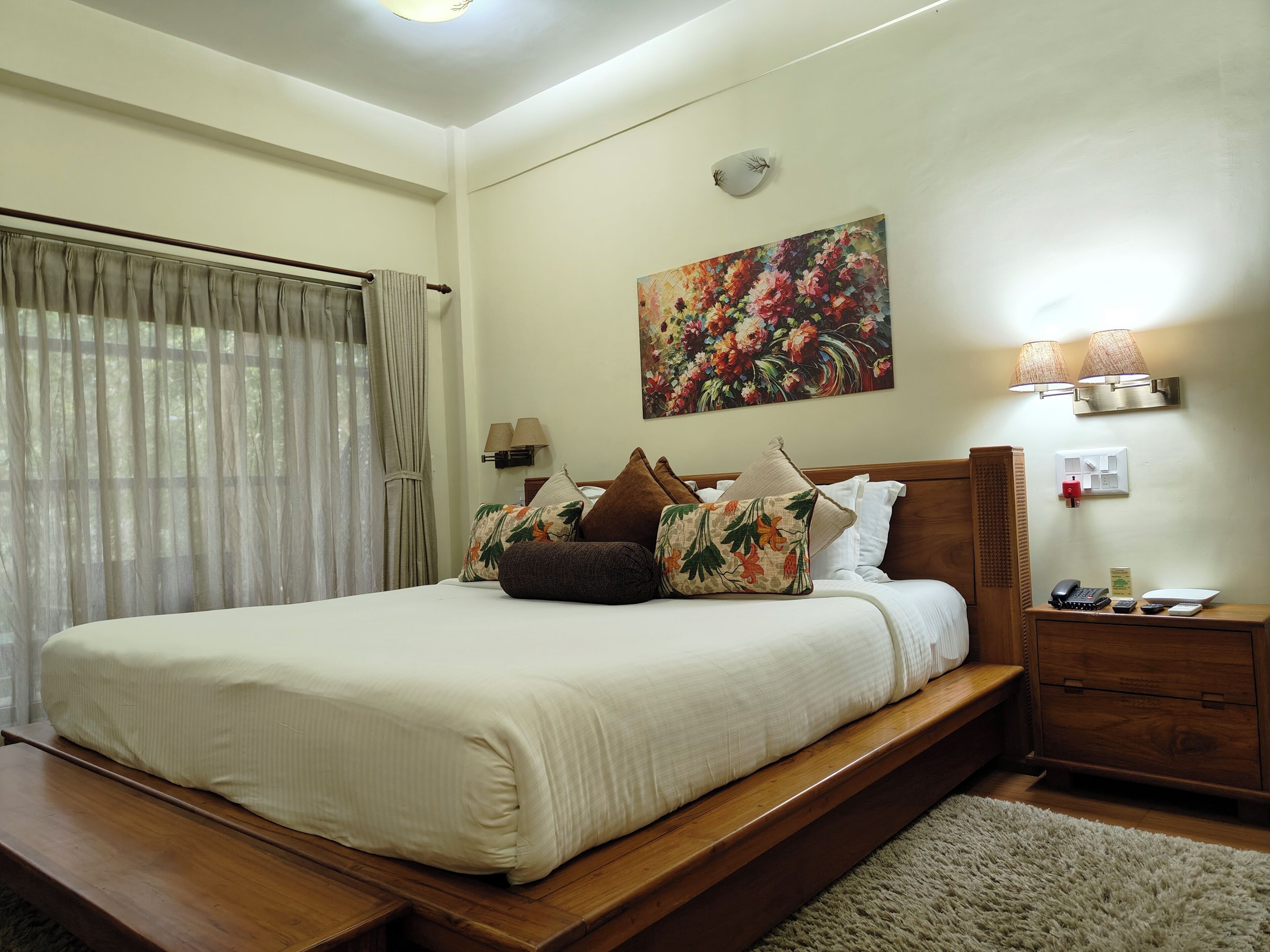 A neatly made bed with a wooden headboard, a bedside table with a lamp, and a painting on the wall.