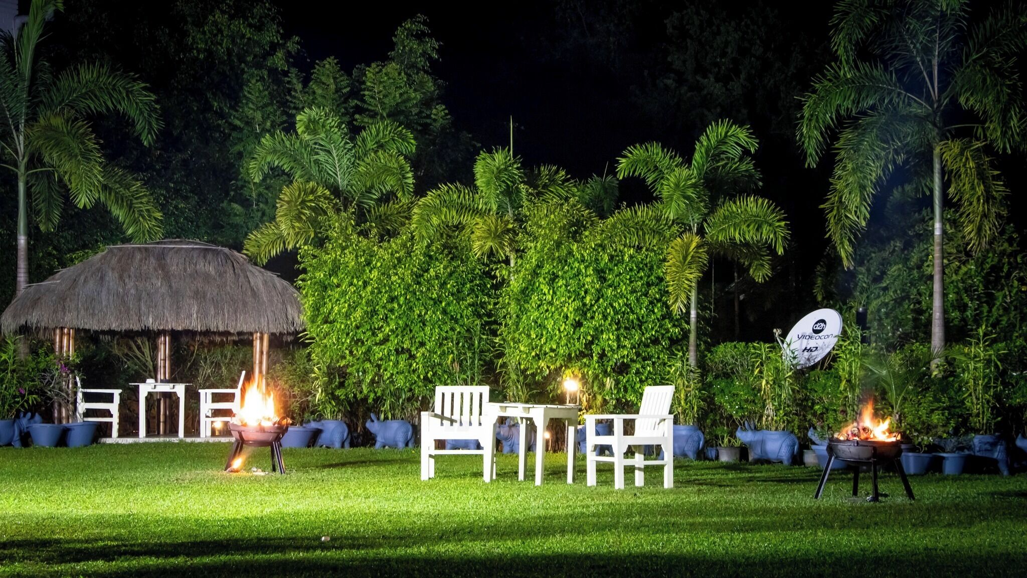 An outdoor seating area with a thatched-roof structure, white chairs, and a satellite dish.
