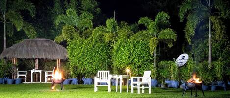 An outdoor seating area with a thatched-roof structure, white chairs, and a satellite dish.