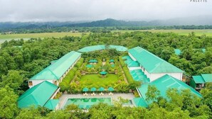 A resort with a central pool, surrounded by lush greenery and multiple buildings with green roofs. - Resort Borgos (Bokakhat)