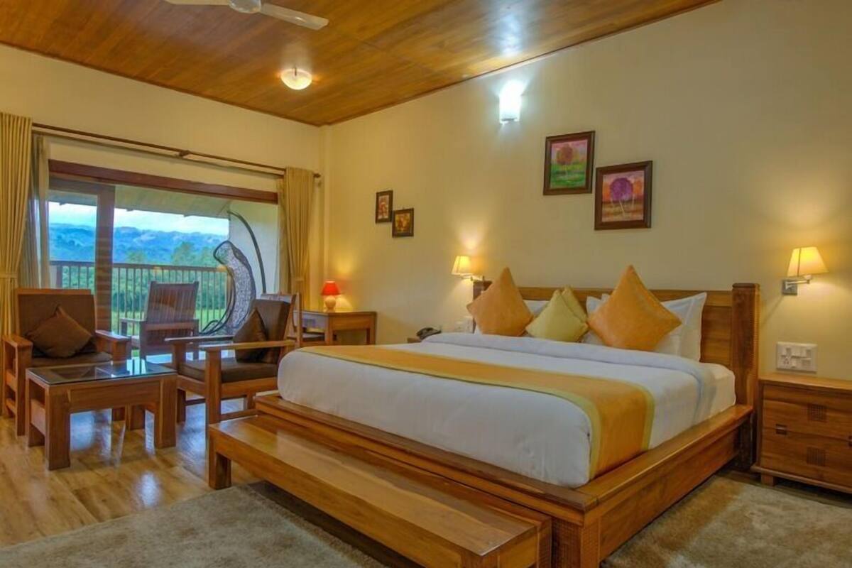 A bedroom with a large bed, wooden furniture, a balcony with a view, and framed pictures on the wall.