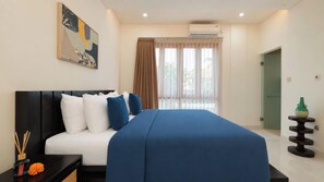 A modern hotel room with a large bed, a bedside table with a vase, and a window with curtains.