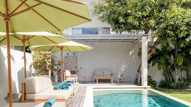 Un área junto a la piscina con una tumbona, una mesa y sombrillas.