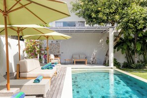 A poolside area with a lounge chair, a table, and umbrellas. - Villa Latima by Villa Finder (Seminyak)