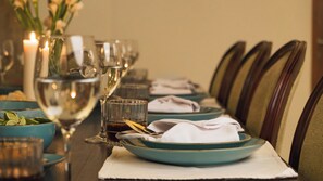 A dining table set with plates, glasses, and napkins, with candles and a vase of flowers in the background. - Villa Latima by Villa Finder (Seminyak)