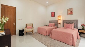 A hotel room with two beds, a chair, a bedside table, a lamp, and a door. - Villa Latima by Villa Finder (Seminyak)