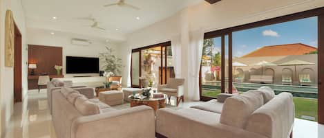 A modern living room with a flat-screen TV, comfortable seating, a coffee table, and a view of a swimming pool and outdoor seating area.