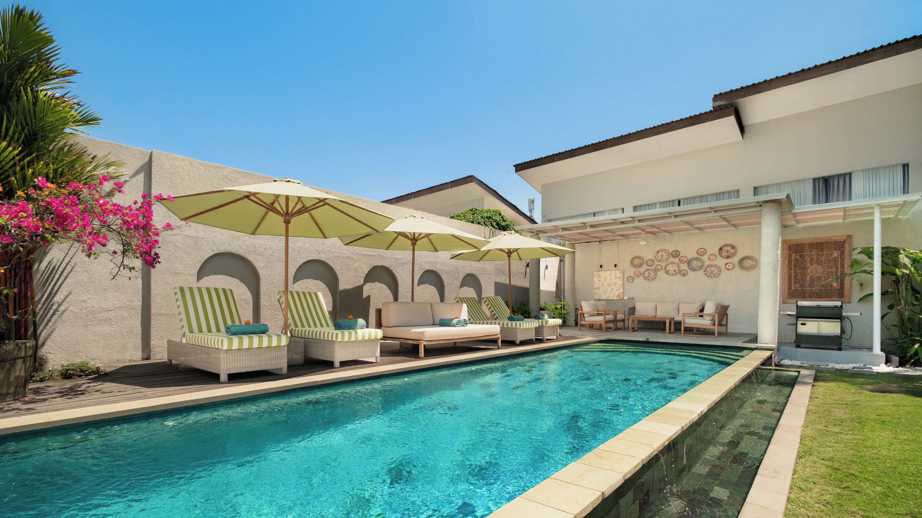Una piscina con sillas de descanso y sombrillas, un espacio de patio con asientos, y una pared decorada con platos.