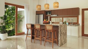 A modern kitchen with wooden cabinets, a marble island, and three wicker bar stools. - Villa Latima by Villa Finder (Seminyak)