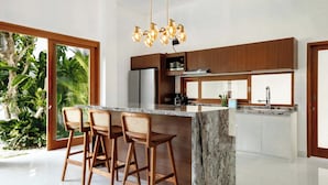 Una cocina moderna con una isla de mármol, taburetes de madera y un refrigerador empotrado.