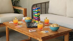 A wooden table with a chessboard, snacks, drinks, and playing cards.