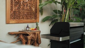 A wooden wall carving, a wooden table with a bottle, a pineapple, and a grill. - Villa Latima by Villa Finder (Seminyak)