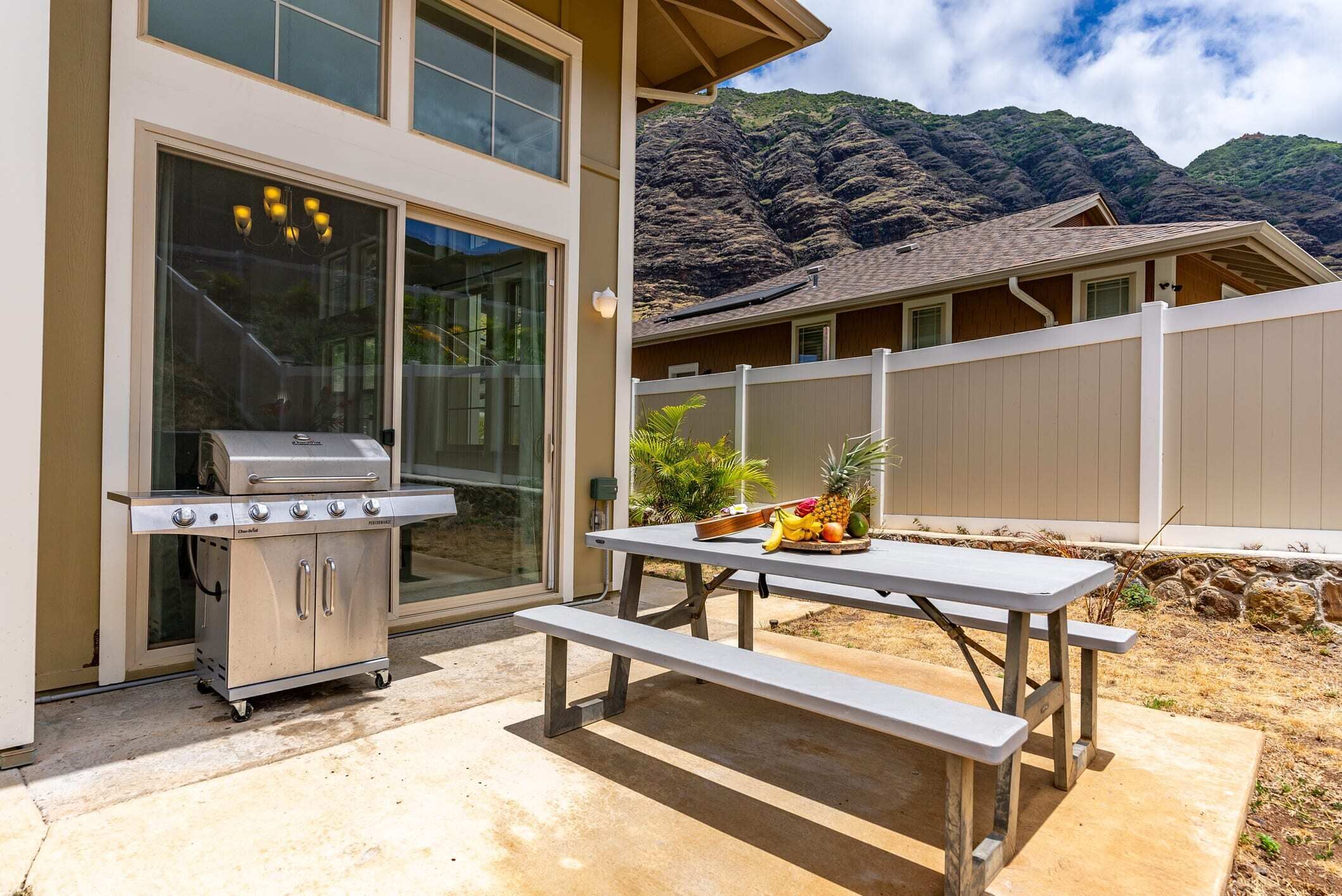 Une terrasse extérieure avec un barbecue, une table de pique-nique avec des fruits et une vue sur les montagnes.