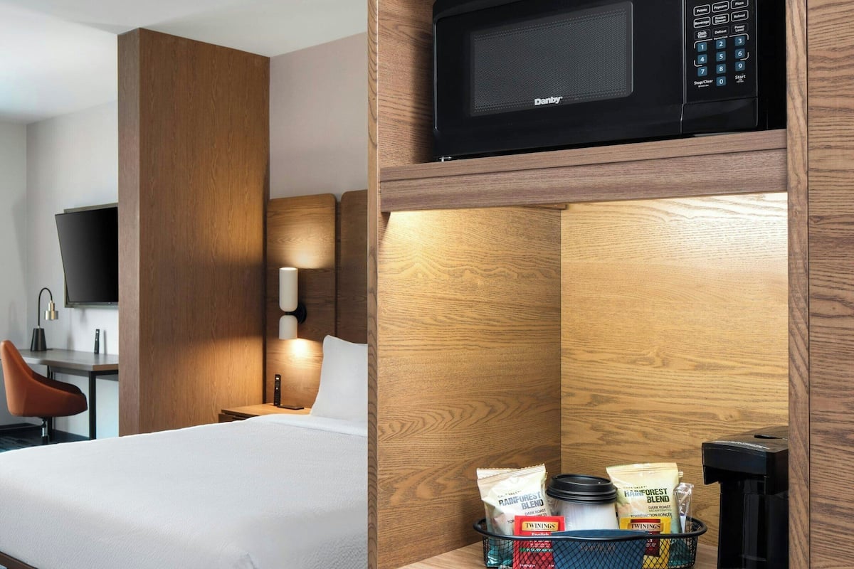 Una habitación de hotel con cama, escritorio con silla, televisor, microondas y cafetera.