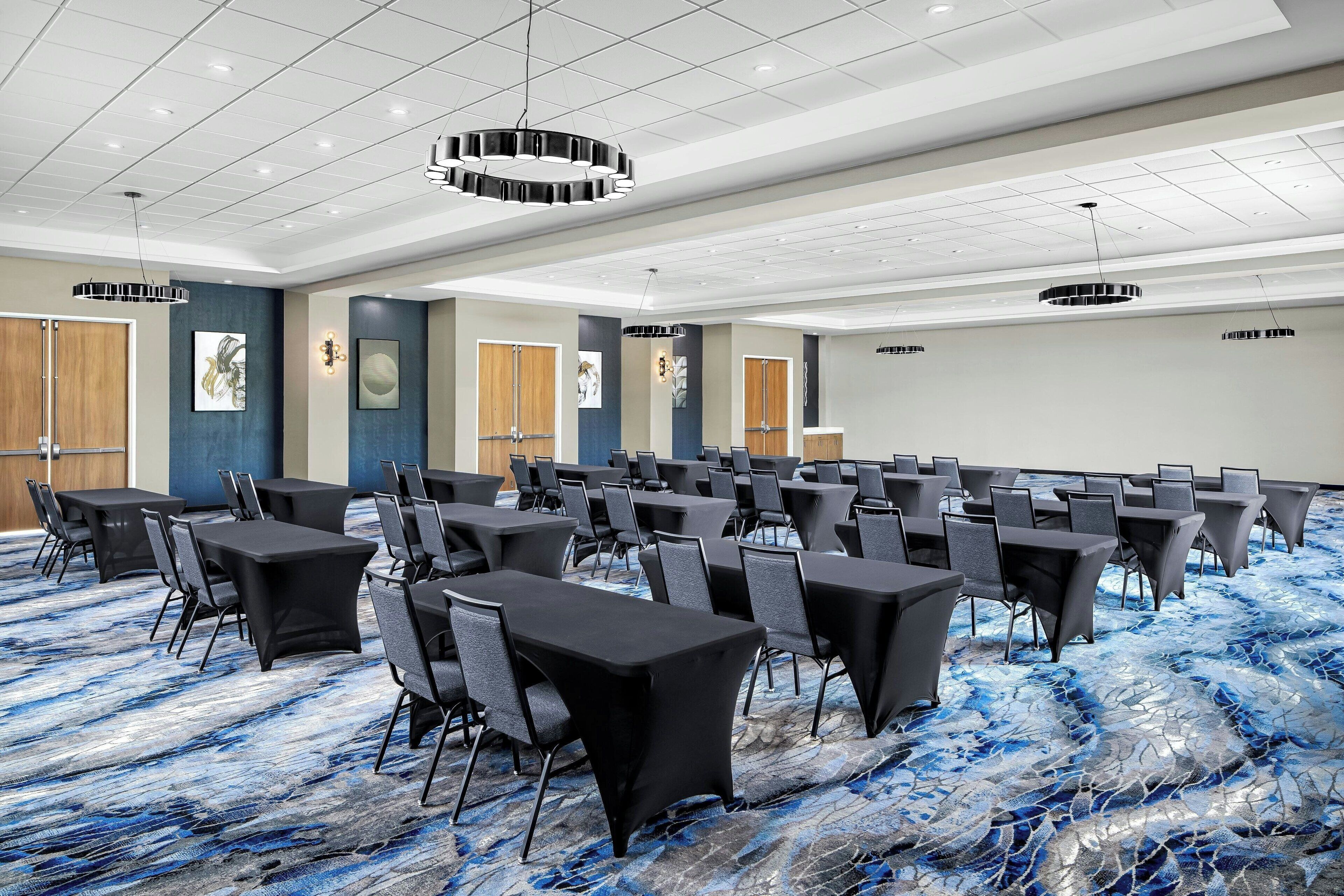 A conference room with multiple tables and chairs, a patterned carpet, and ceiling lights.