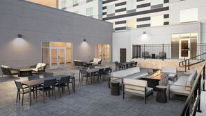 Un espace extérieur aménagé en terrasse, avec différents coins salon, comprenant des tables et des canapés, ainsi qu’un foyer central.