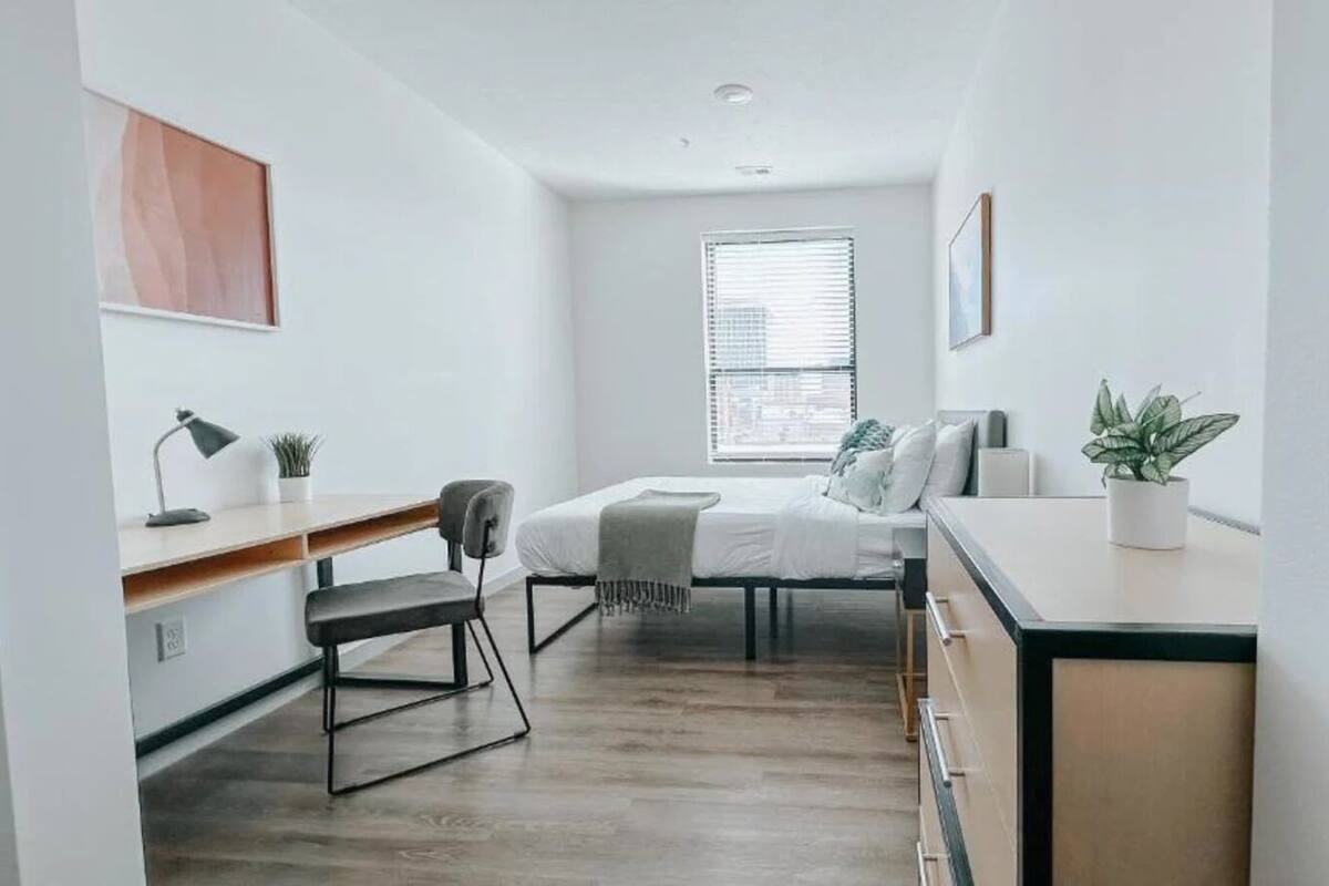 A small, modern bedroom with a bed, bedside table, chair, and a desk.