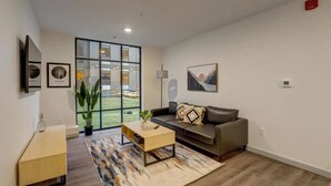 A modern living room with a grey sofa, a coffee table, and a large window offering a view of a green outdoor area. - Stay on M Street (Lincoln)
