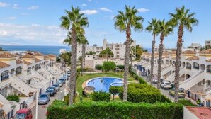 A coastal residential area with a swimming pool surrounded by palm trees and white buildings with terracotta roofs. - Bungalow Avec Solarium à 5mn des Plages (Gran Alacant)