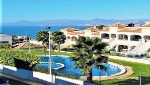 A resort with a swimming pool, palm trees, and a view of the sea and mountains. - Bungalow Avec Solarium à 5mn des Plages (Gran Alacant)