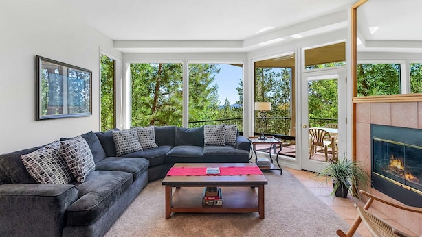 A modern living room with a sectional sofa, a coffee table, and a fireplace. Large windows provide a view of the outdoors. - Frosty Summit Condo at Mount Bachelor Village (Bend)