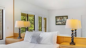 A hotel room with a bed, two bedside lamps, a painting on the wall, and a window with a view of trees. - Frosty Summit Condo at Mount Bachelor Village (Bend)